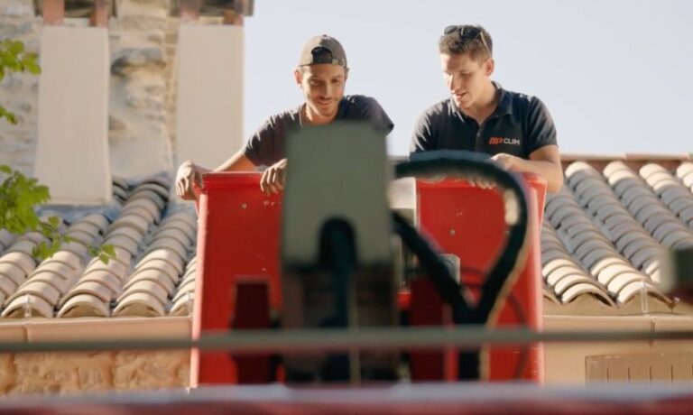 Deux techniciens MP Clim, installateurs de climatisation à Orange, positionnant une unité depuis une nacelle élévatrice sur toit en tuiles provençales.