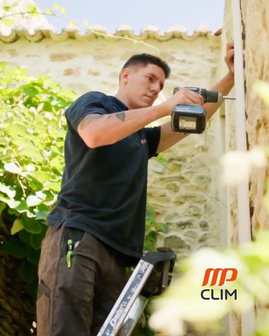 Installateur de climatisation à Orange fixant les supports d'une unité extérieure sur mur en pierre, perçeuse à la main, échelle en aluminium.